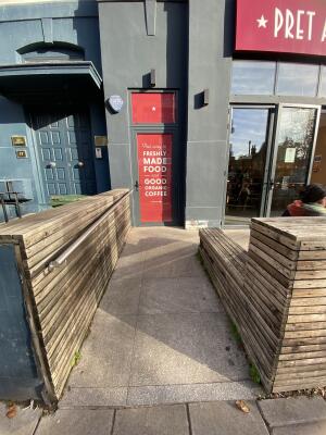 From sidewalk facing the venue. Pathway ahead with silver metal handrail on left. Entrance door at back right.
