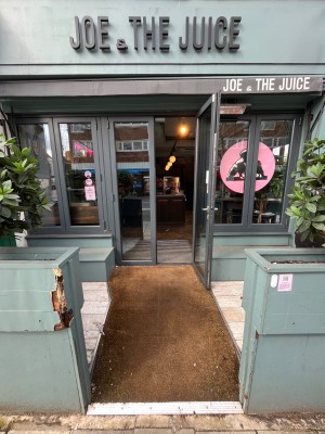 From sidewalk facing venue. Opening ahead. Fences on left and right. Door at back.