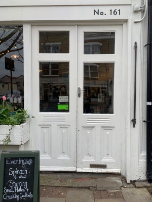 Glass doors with white wooden frames ahead. Push handle in centre to open. Signboard on left.