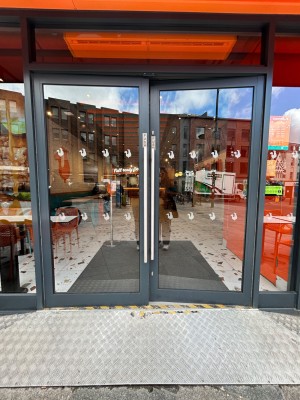 Double glass doors with dark grey frames. Push vertical silver handles in middle to open.
