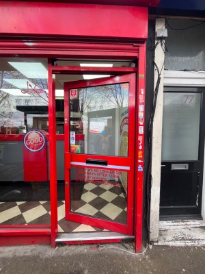 Single glass door with red metal frame. Red metal handle. Push from left to open.