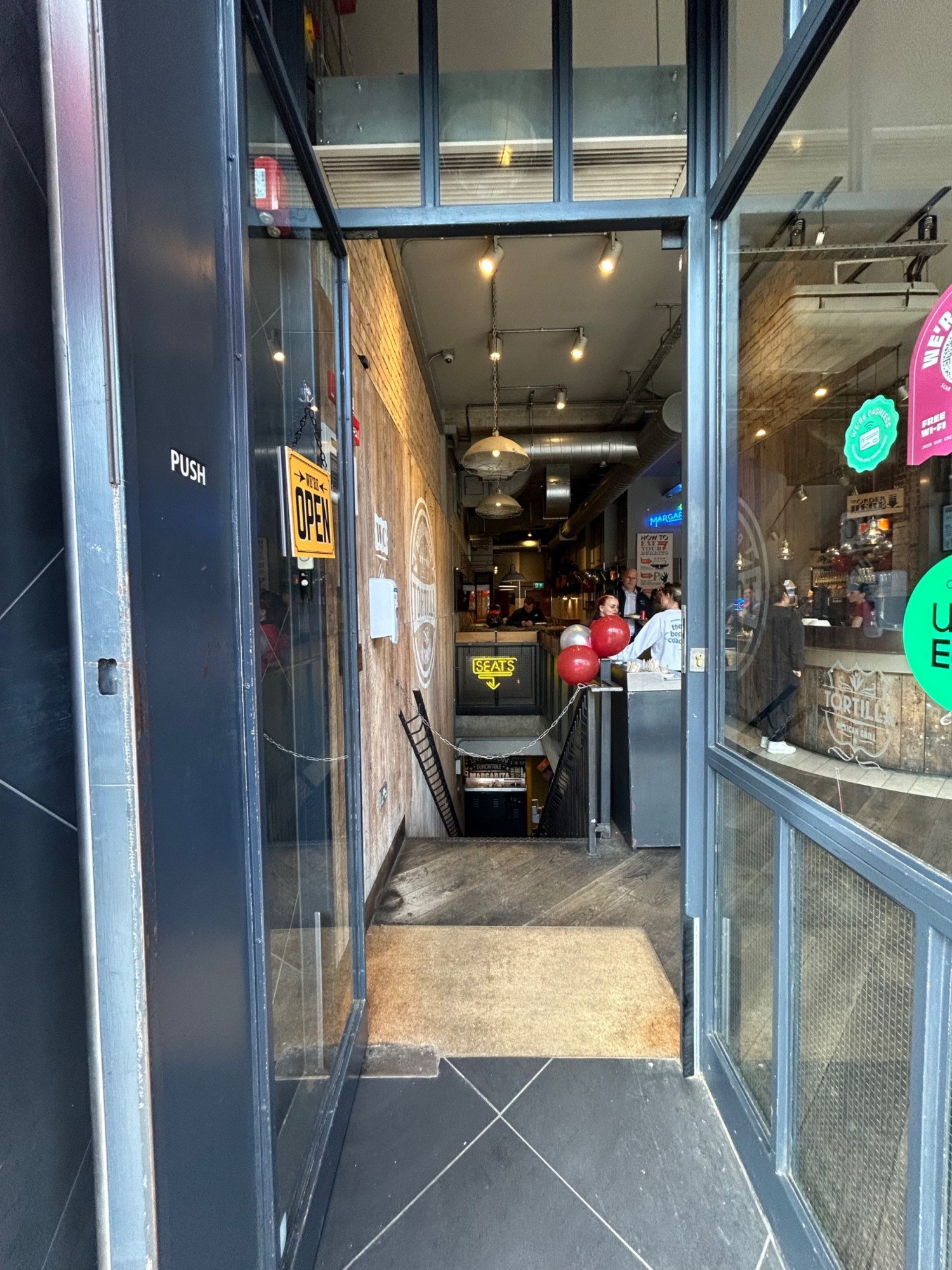 From archway, facing straight. Grey wooden single door with large glass panel. Pull from right to open.