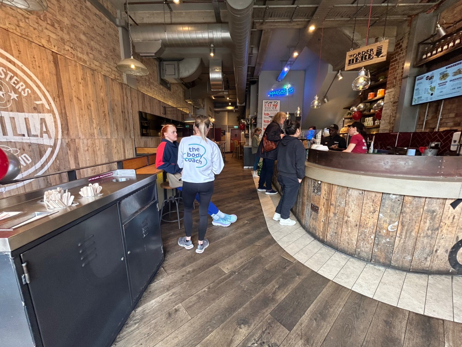 From start of counter, facing straight. Path ahead. Counter runs along right wall. High table and stools along left.