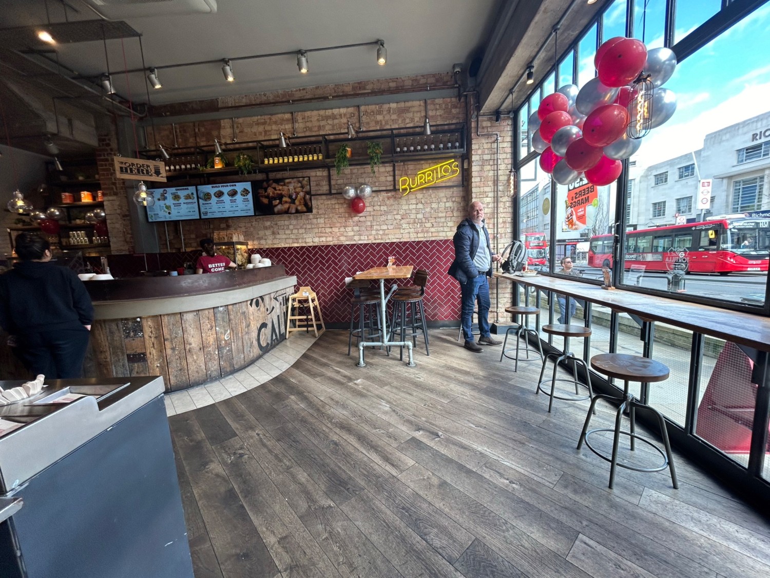 From entrance, facing right. Path ahead leads to high tables and stools along right wall and back. Counter starts on back left.
