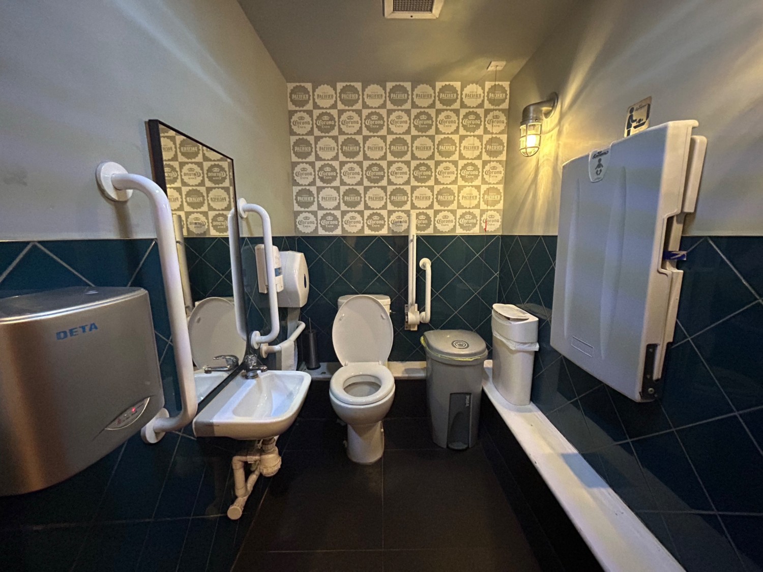 From doorway, facing straight. Sink on left wall. Toilet on left of back wall. Pull cord on right of back wall. Baby change on right wall.