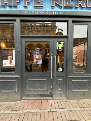 Glass panelled door in black wooden frame. Silver handle to right of door. Push to open.