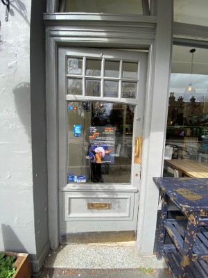 Glass door, with grey doorframe. Golden handle on right. Push to open.