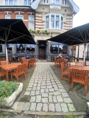From street, looking at venue. Path to entrance ahead. Tables and chairs on both sides.
