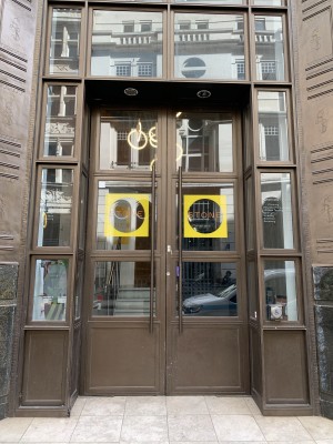 wide heavy double doors with glass panels and horizontal bar handled in the middle, slight incline ramp from pavement, wheelchair button on the right