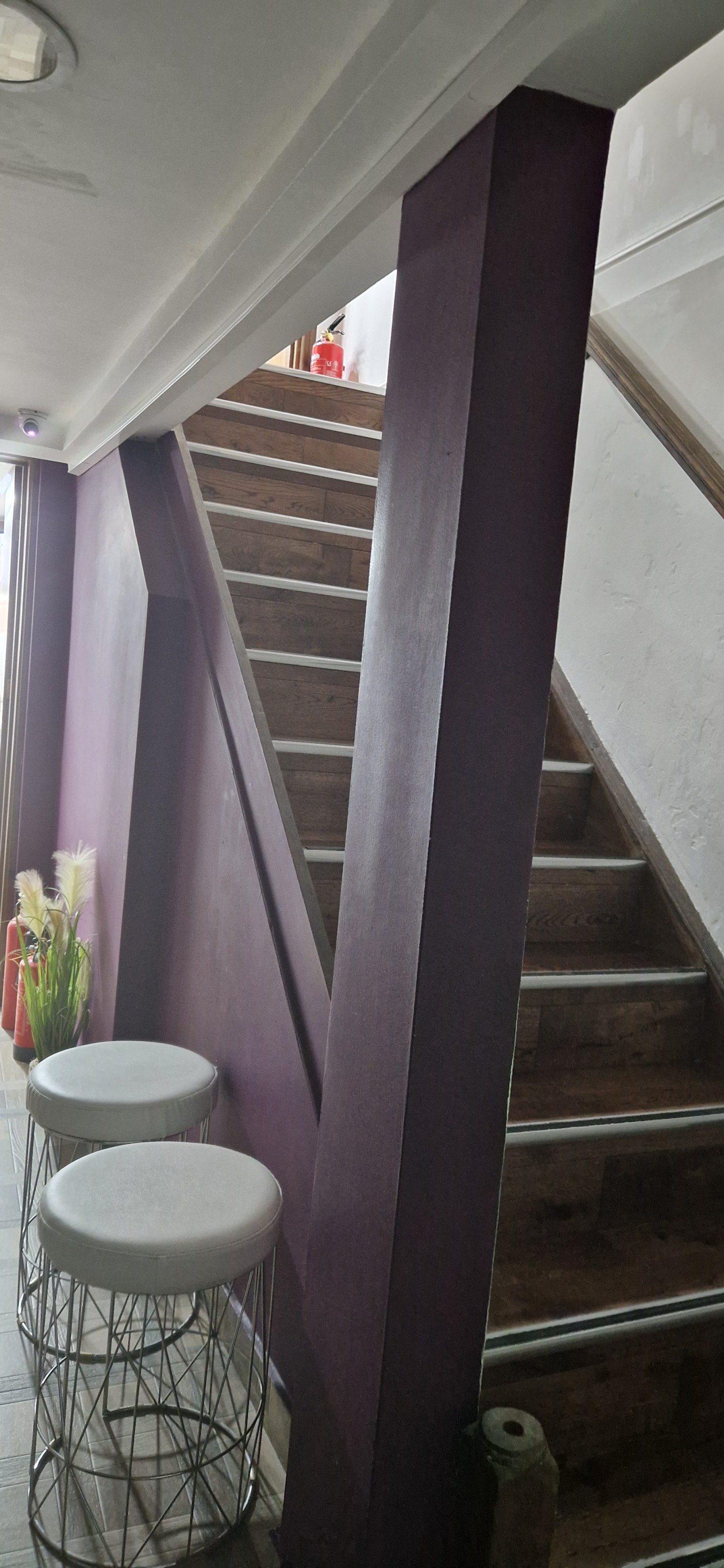 View of stairs to toilet from the bottom. Handrails on the left, no wall on the right. Stairs are normal height and metal strip to show the steps.