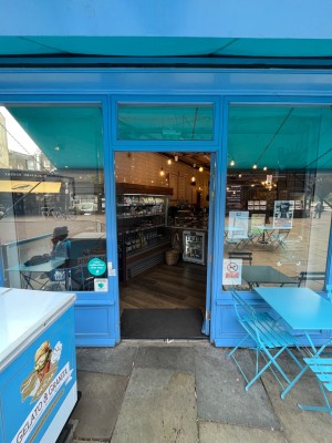 Blue framed glass door, push via handle on left to open. Doorbell on left of doorframe.