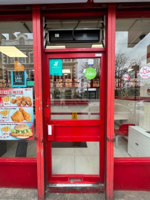Red framed glass door. Push via handle on left to open.