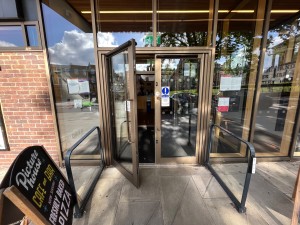 Brown framed glass doors, open via push button. Button is on right railing before door.