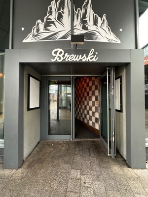 From pavement facing first set of glass double doors with grey doorframe. Silver handles towards centre of doors. Pull to open.