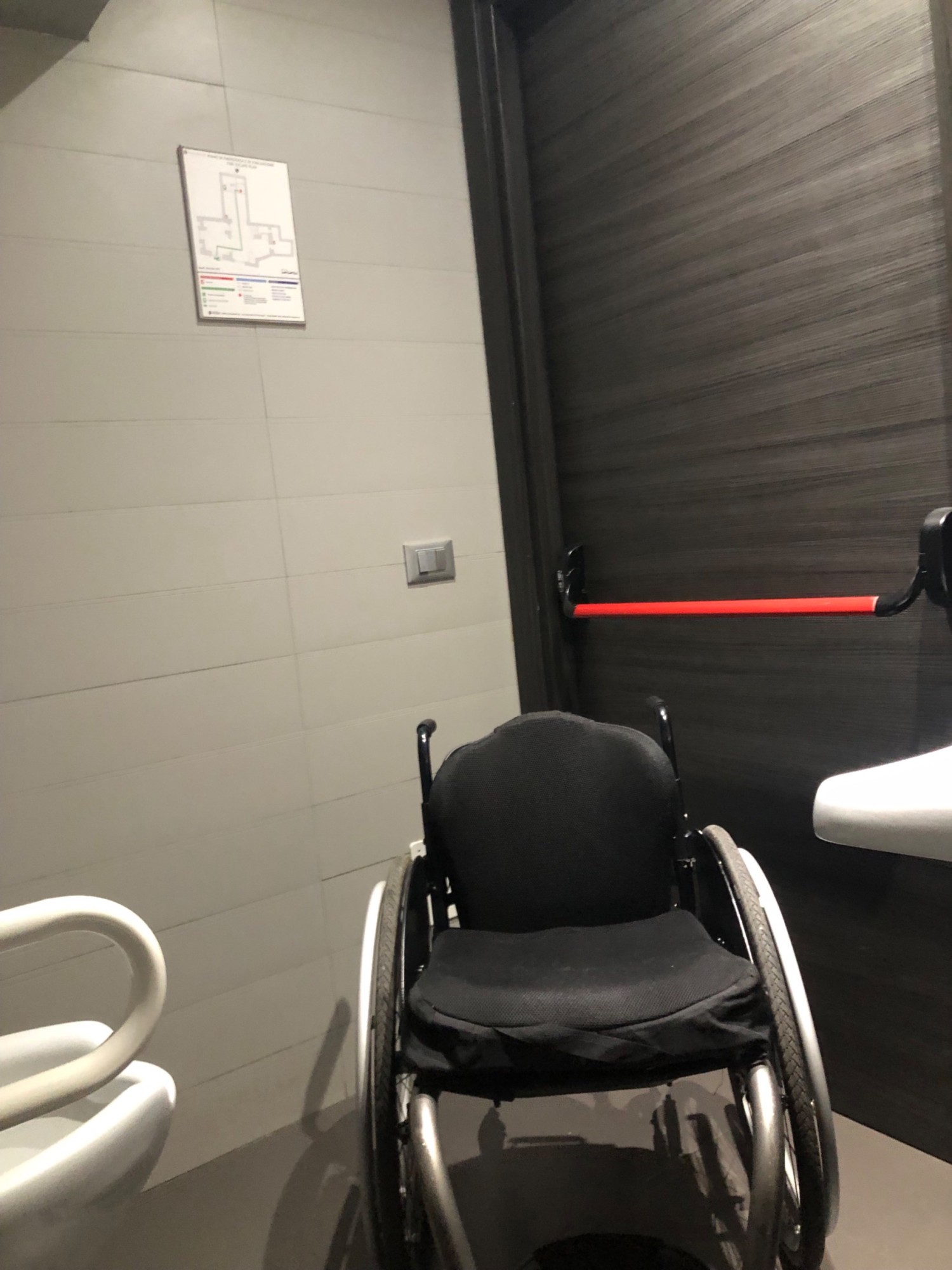 The door, which has a bar to push to exit
It also shows that the space in the bathroom is limited, my “average size” wheelchair is size reference