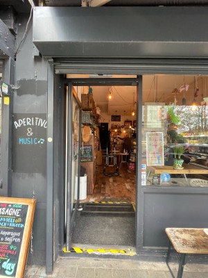 Black glass door, with handle on right. Push to open. Sign board at left, bench at right of the entrance door.