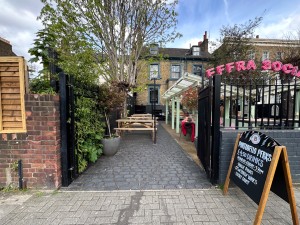 From street facing venue, black double gate ahead. Push from center to open. Path straight to outdoor area and entrance.