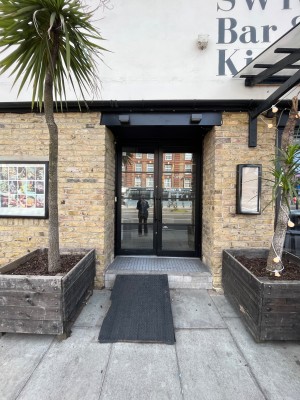 From pavement facing venue. Path to entrance proceeds between two planters ahead.