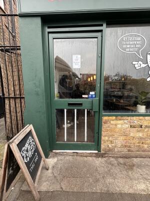Green glass door with green metal frames ahead. Push from right to open. Display board at left of entrance.
