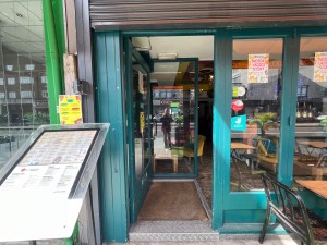 Single glass door with blue wooden frame. Silver metal handle. Push from right to open. Sign to left.