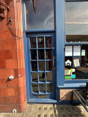 Single glass door with blue wooden frame. Gold metal handle. Push from right to open.