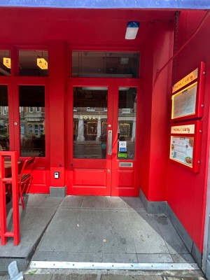 Built in ramp, then single bright red wooden door with large glass panel ahead. Pull silver vertical handle on right to open.