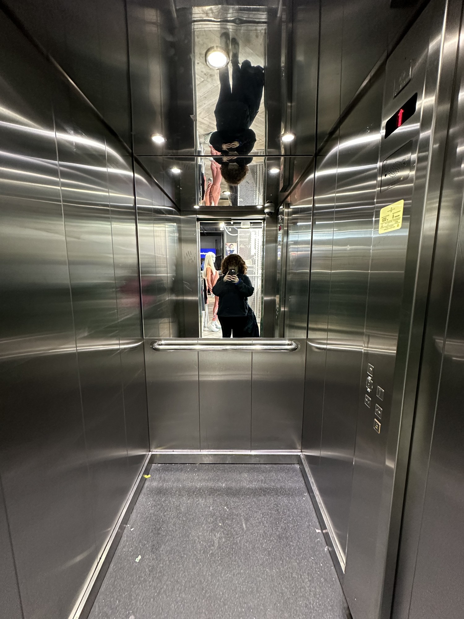 From lift doors looking inside. Horizontal grab rail along back wall, with mirror above. Button panel on the right.