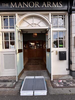 Grey metal wheelchair ramp available upon request to white framed glass doors. Pull metal handles in centre to open. Doorbell on right of door.
