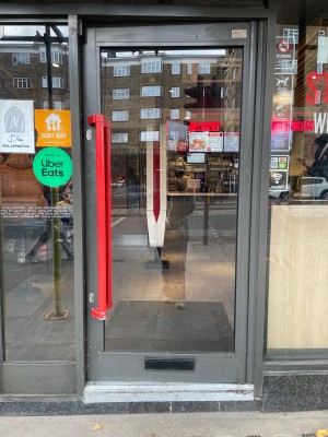 Single glass door with grey frame. Push red vertical handle on left to open.