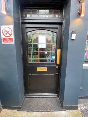 Black wooden door, with glass panel. Gold push metal plank on right. Push to open.