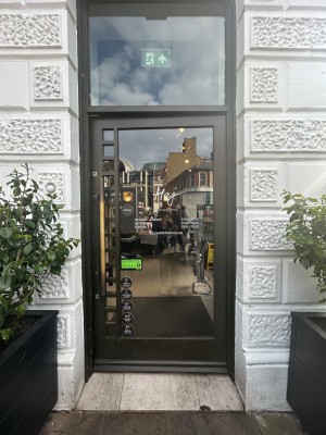 Single glass door with dark brown frame. Push gold vertical handle on left to open.