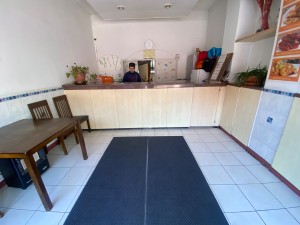 From entrance, facing straight. Carpeted path ahead to counter. Counter along back wall. Table and chairs along left wall.
