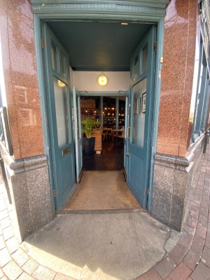 Blue wooden double door, with glass panels. Golden handle at centre of door, on right. Push to open.