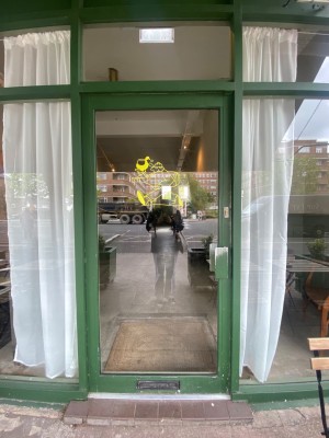 Glass door, with green doorframe. Handle on right. Push to open.