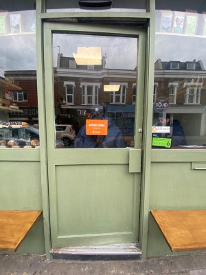 Glass door, with green doorframe. Handle on right. Push to open.