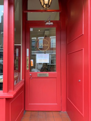 Red wooden door with glass panel. Push from gold metal handle on left side of door to open.