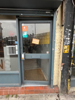 Grey framed glass door. Push open via handle on left.