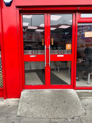 Ramp up to red framed glass double doors. Vertical silver handles in the centre. Push to open.