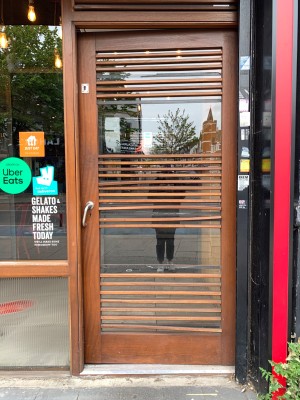 Glass door with brown wooden frame. Push from silver metal handle on left of door to open.