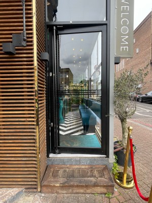 Single glass door with black metal frame. Push metal handle on left to open.