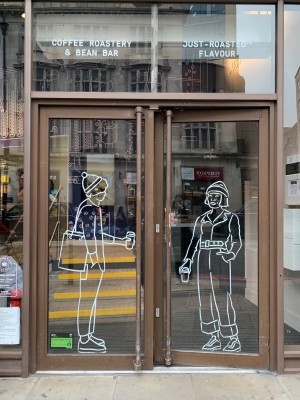 Double glass doors with brown metal frames. Push from handles in centre to open.