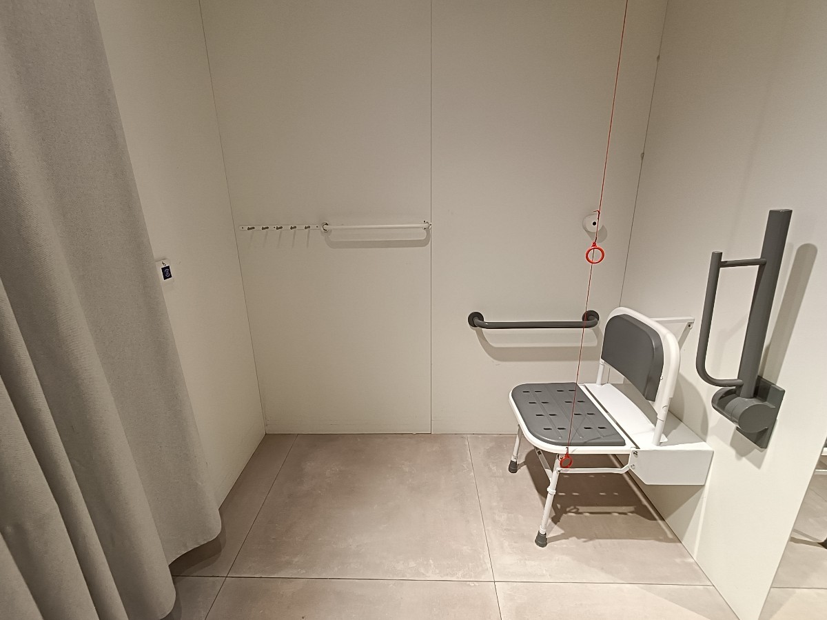 From after curtain, looking left. Folding chair at back right. Emergency pull cord to it's left. Emergency call button on left wall.
