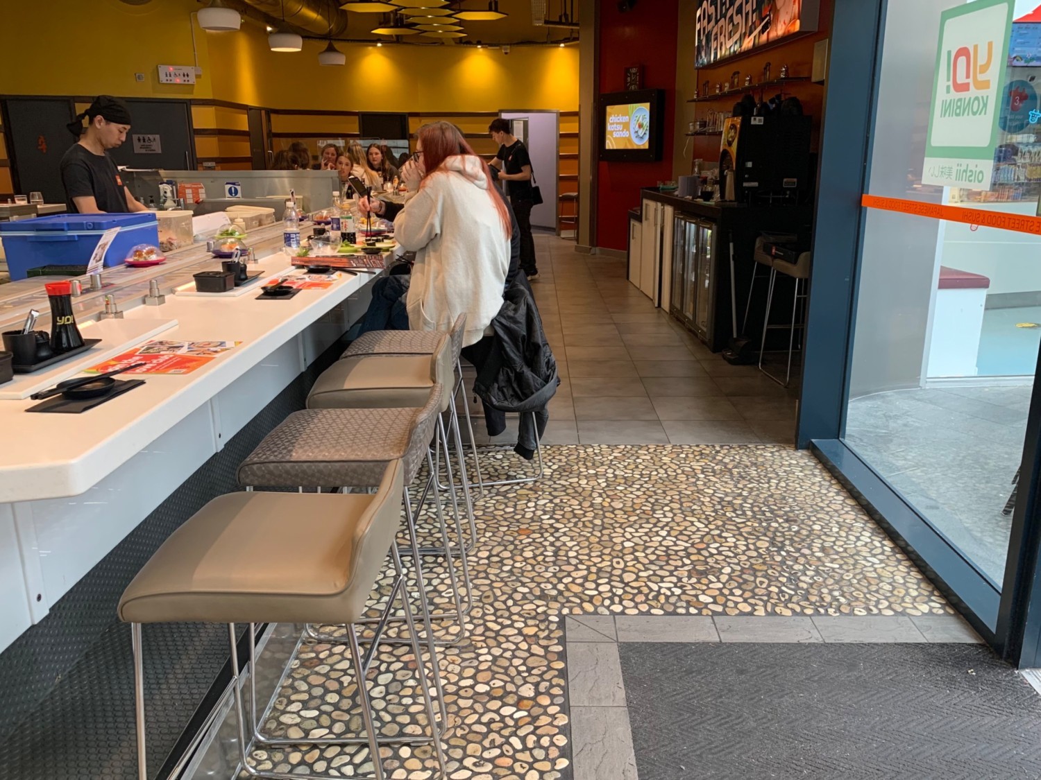 From corner of sushi train facing left. High table and stools continue along left. Condiment stand to back right.