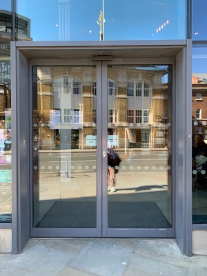 Double glass doors with grey metal frames. Automatic doors slide open from centre.