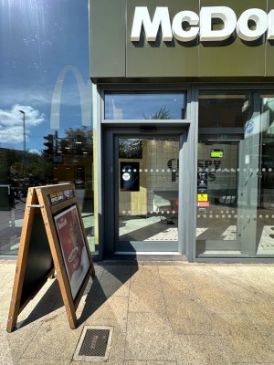 A-frame to the left ahead of the entrance. Glass automatic door with grey doorframe. Slide to right to open.