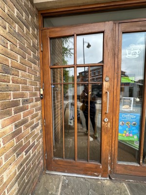 From pavement looking straight at first glass panelled door with wood doorframe. Silver handle to right of door. Pull to open.