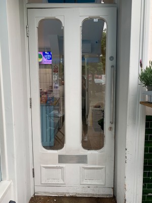 White wooden door with glass panels. Pull from silver metal handle on right of door to open.