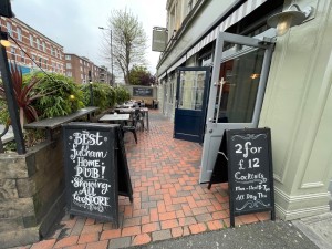 From street, facing venue. Signs on left and right. Path in between. Entrance on right wall after signs.