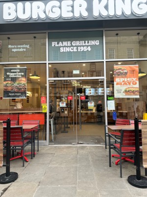 Outdoor tables and chairs with a gap to access two glass doors. Long, metal handles are prominent. The entrance is flat level. A doorbell is available
