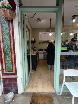 From sidewalk facing venue. Green framed glass door ahead. Push handle on right to open inwards.